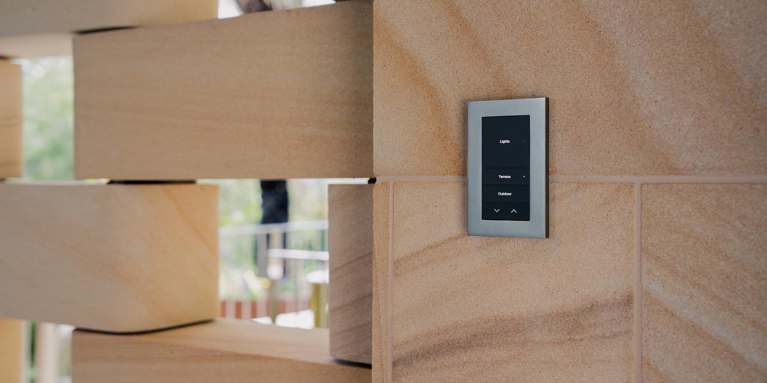 Wall-mounted smart lighting control panel on tan brick wall